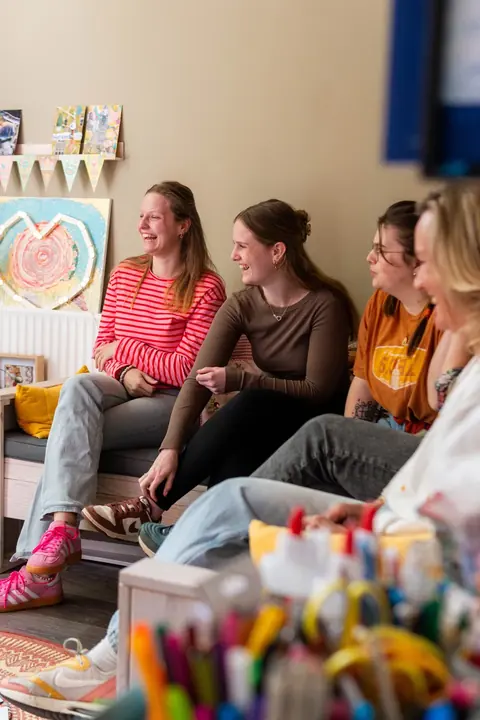 Een groep professionals zit lachend samen tijdens een bijeenkomst.